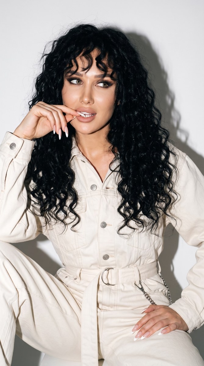 Curly-Haired Woman in a Cream Balenciaga Jumpsuit